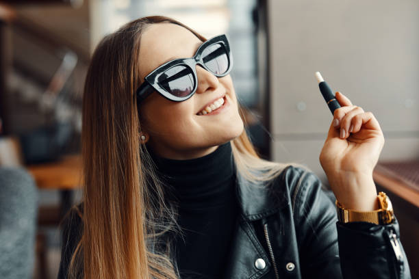 Girl sit in caffee place and smoke electronic cigarette wear glasses